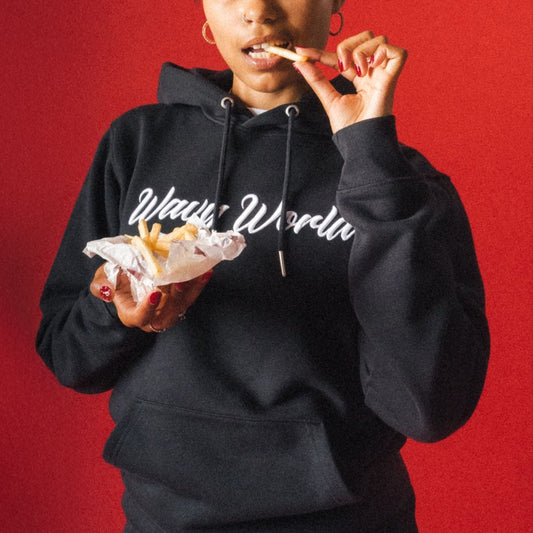 Person wearing the black Wavy World OG Hoodie from Drop 1 - Hip Hop & Cereal, featuring bold text, eating in front of a red background
